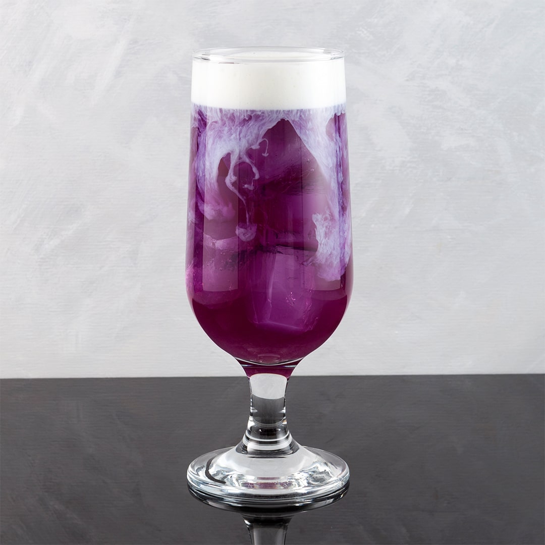 Purple cocktail with white foam in a glass on a gray surface and background
